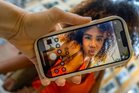 Hand holding smartphone showing woman with curly hair puckering for a selfie on the front camera,