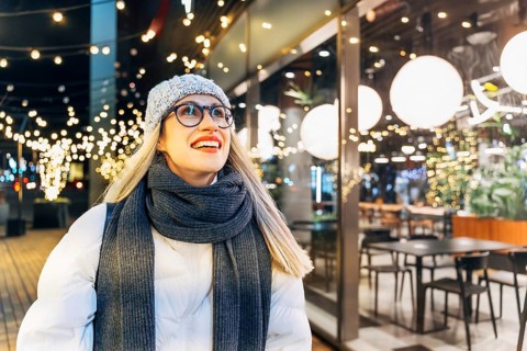 Young woman enjoying festive lights in winter evening. A woman wearing a light gray knit hat,