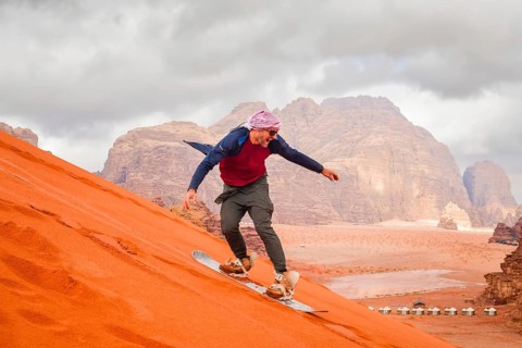Man successfully sandboarding down steep red dune in Wadi rum showing skill balance confidence