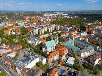Aerial view of a city with various churches and buildings surrounded by green spaces under a blue