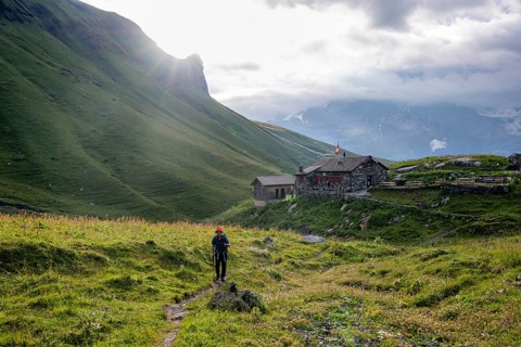 Hiker on a hiking trail, behind mountain lodge Rotstockhütte in front of a mountain landscape,