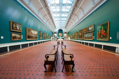 A long gallery space with paintings on green walls and benches under a skylight, National Gallery