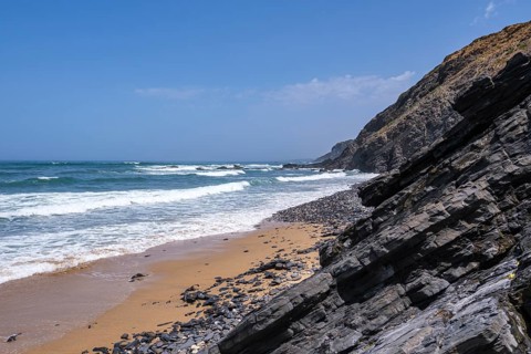Rocky cliffs stretch along a sandy beach, ocean waves crash against the coast, Rogil, Faro,
