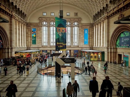 View of the main hall of Leipzig Central Station with passers-by and advertising posters, train