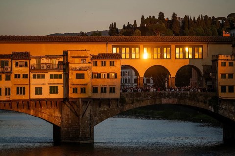 Warm evening light falls on the historic Ponte Vecchio segmental arch bridge across the Arno River
