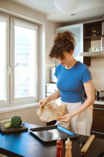 Woman is handling parchment paper near a baking tray. Natural light brightens the space