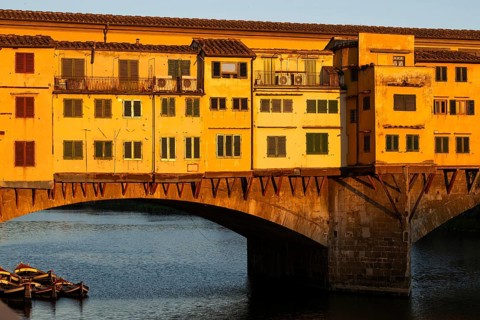 Wooden boats, Arno river, warm evening light on the historic Ponte Vecchio segmental arch bridge,
