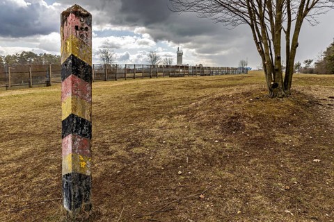 A colorful landmark stands in a meadow with a tree and a distant watchtower in cloudy skies, the