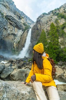 Woman hiker wearing a yellow jacket and beanie enjoying a breathtaking view of lower yosemite falls
