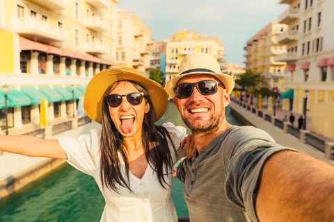 Happy tourist couple taking selfie Qanat Quartier Doha. Woman sticking tongue out, man smiling,