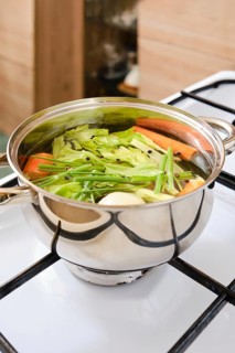 Fresh vegetables are being cooked in a pot on a stove. Cooking vegetable broth