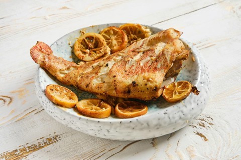 Roasted whole red snapper is placed on plate along with roasted lemon slices. Fish ready for