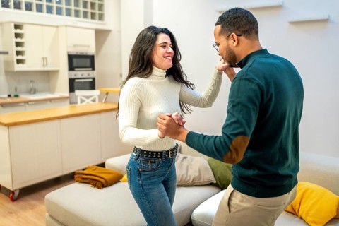 Happy young couple laughing and enjoying a romantic dance together in their modern apartment,