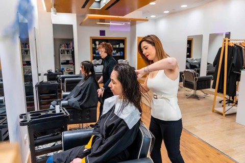 Professional hairdresser working on a customer's wet hair with a comb while another stylist attends