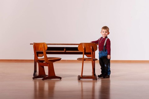 Little boy standing next to an old wooden school desk in an empty room, generated by AI