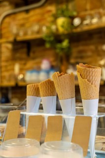Waffle ice cream cones are neatly stacked in a display stand with blank brown labels on a serving