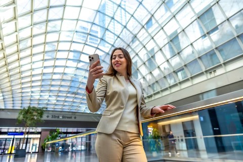 Young businesswoman standing in a modern transportation hub, smiling while looking at her