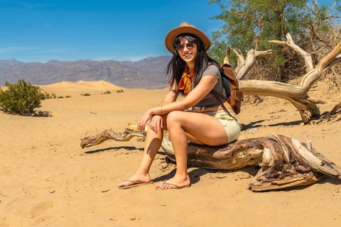 Woman in adventure attire sitting on sun bleached driftwood, taking a break from exploring the vast