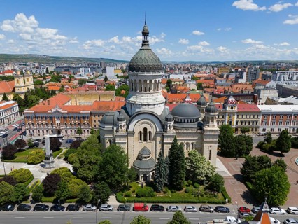 Large church with eye-catching tiled roof nestled in an urban environment with green spaces, aerial
