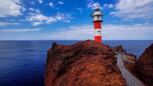 Punta de Teno, red and white lighthouse stands on rugged rock with a wide view of the sea, Masca,