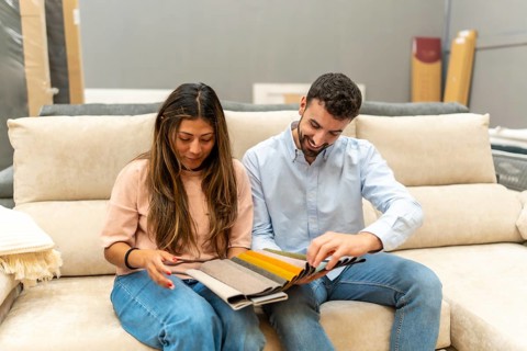 Diverse young couple on a sofa comparing colorful fabric samples and swatches in a modern furniture