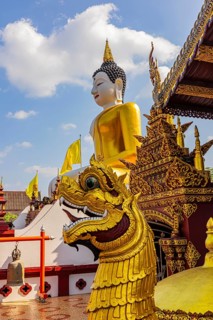 Huge gilded sitting Buddha, in front of a mystical dragon head, in front of the Buddhist temple