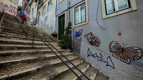 Butterfly graffiti on a wall next to a steep paved stone staircase, a person running up, Lisbon,