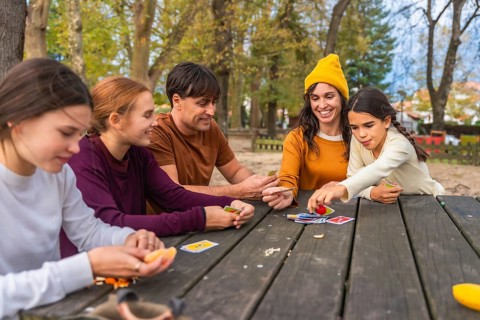Family members, including parents and children, are sitting at a rustic picnic table in a park,