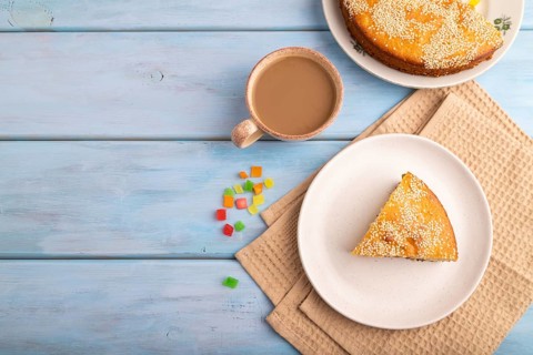 Pie with candied fruit, cup of coffee, on blue wooden background with beige textile, copy space,