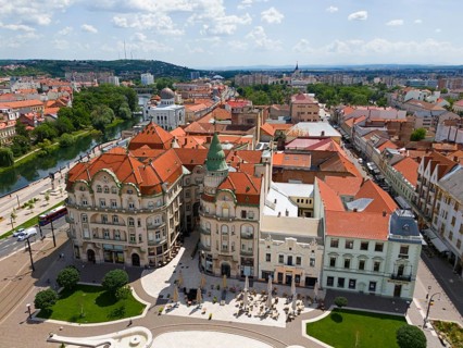 Aerial view of buildings with red roofs and green tower in a hilly cityscape near a river, aerial