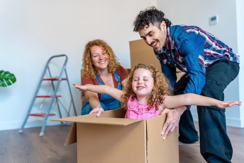 Happy family unpacking in their new home, parents having fun with their daughter playing inside a