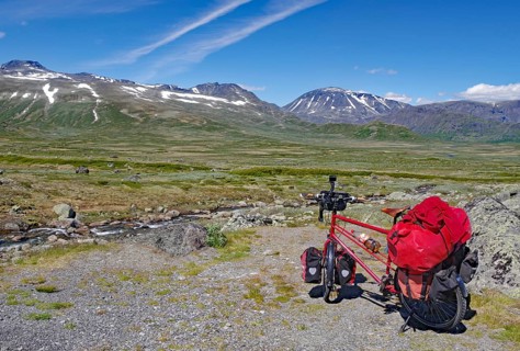 Loaded bike in front of a vast mountain landscape with blue sky and individual clouds, bicycle