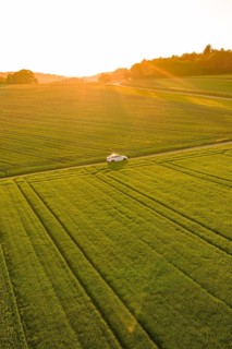 A white car drives along vast green fields in the light of a low sunset, Tesla Model Y, Gechingen,