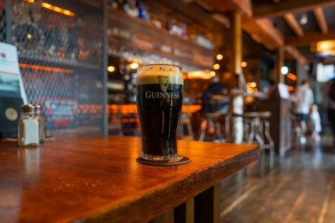 A filled Guinness glass on a wooden table in a warm bar atmosphere, Nightlife, Dublin, Ireland