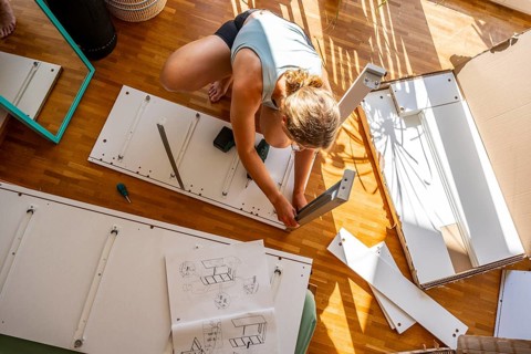 Young woman setting up a shelf, furniture assembly with screwdriver, IKEA furniture in a new