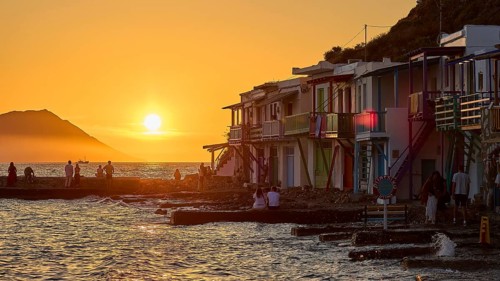 Coastal buildings at sunset with warm light and people as silhouettes on the water, boathouses,