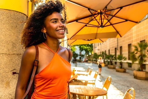 Happy young woman with curly hair smiling and looking away, enjoying leisure time at an outdoor