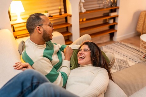 Young couple relaxed on a cozy sofa at home, sharing laughter and warm conversation in a bright