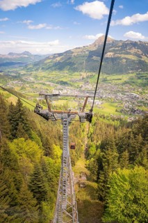 Cable car high above a wooded slope with views of a valley and mountains in the distance,
