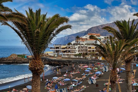 Puerto de Santiago, popular black sandy beach with many sun worshippers and palm trees by the sea