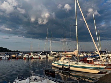 Yachts in harbor under dramatic cloudy skies, calm water and soft evening light create a peaceful