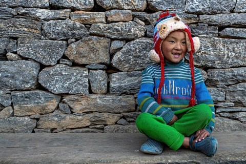 Happy smiling little Nepalese boy from the Sherpa ethnic group sitting in front of stone wall, Solu