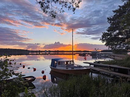 A boat is moored on a jetty in a calm lake at sunset with glowing clouds and reflections in the