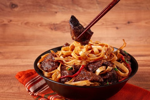 Udon noodles with beef in Mongolian style, with green onions and vegetables, served in a black
