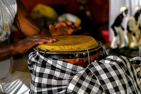 A drummer playing a traditional atabaque drum decorated with cloths during an Umbanda celebration