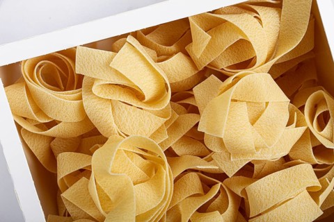 Raw pappardelle pasta, pasta nests, in a paper box, top view, no people