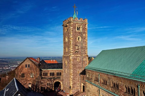 Castle ensemble with a high tower and several buildings with green roofs under a blue sky, The