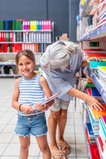 Grandmother and young granddaughter selecting colorful notebooks and stationery items from a store