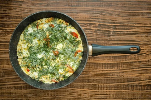 Top view of frying pan with omelette with tomatoes, ham and herbs on wooden tabletop