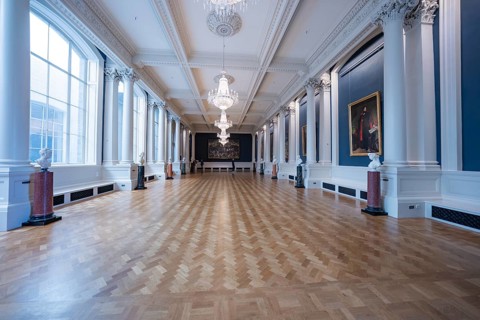 A spacious classic gallery room with parquet floors and high ceilings, decorated with paintings and